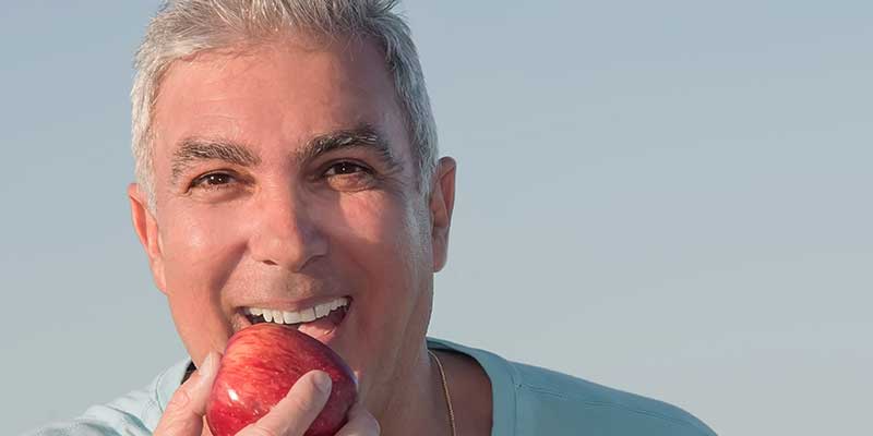 man with dental implant eating an apple